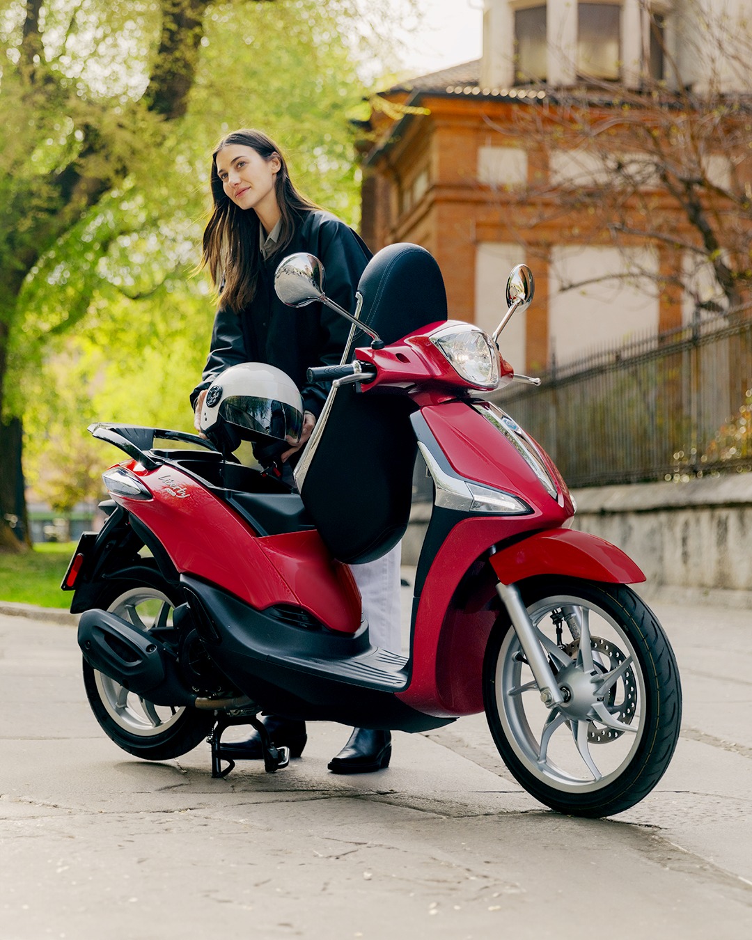 Mujer posando con un scooter Piaggio de color rojo en un entorno urbano