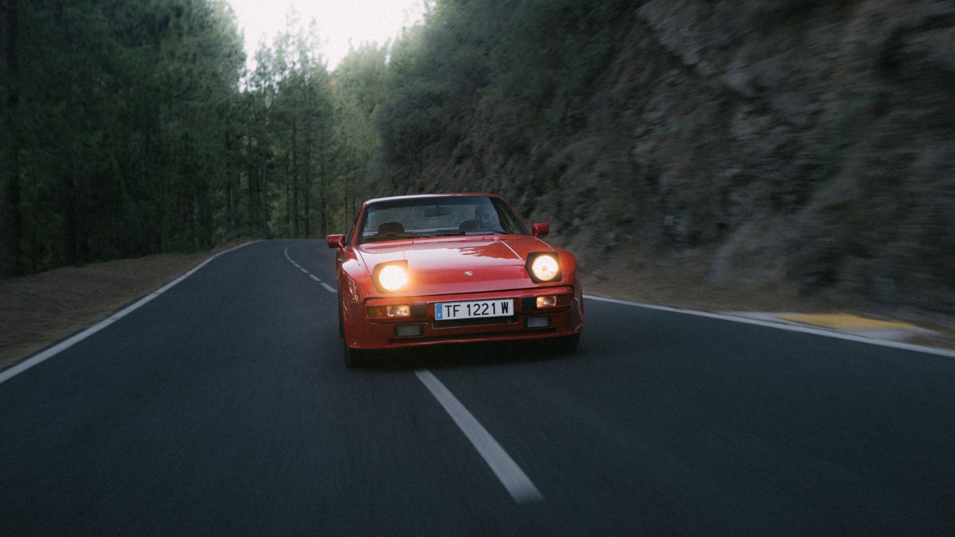 Vista dinámica de un Porsche 944 en tono rojo circulando por una carretera forestal.
