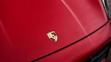 Primer plano del emblema de Porsche en el capó de un Cayenne GTS 2024, resaltando su prestigio.