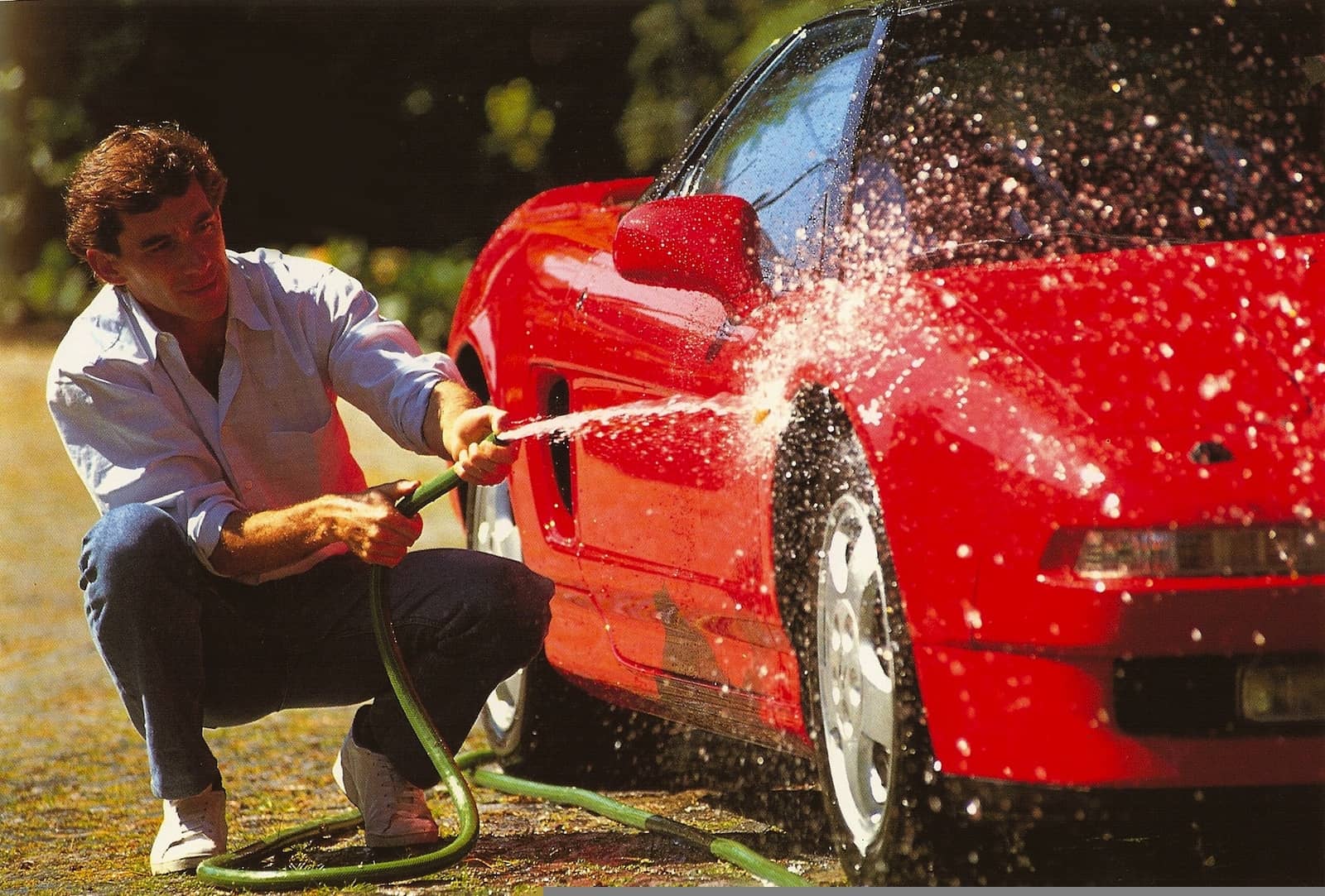 Imagen de Ayrton Senna lavando un Honda NSX rojo, destacando la figura del deportivo.