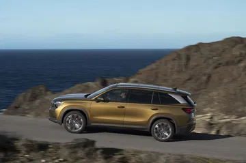 Vista lateral del Skoda Kodiaq 2024 en carretera con fondo de mar y rocas.