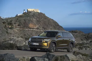 Vista delantera y lateral del Skoda Kodiaq 2024 en carretera con un paisaje montañoso al fondo.