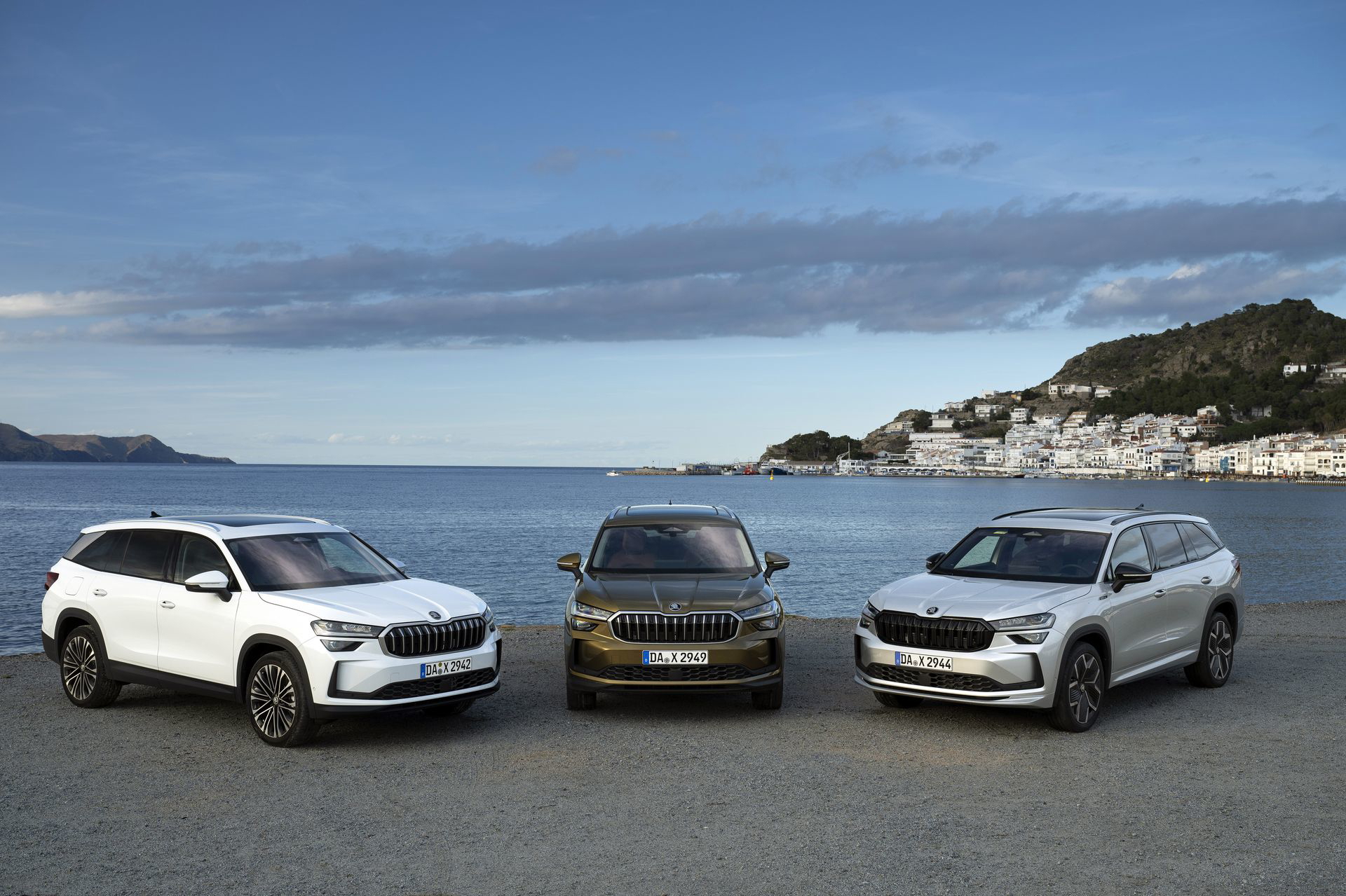 Tres modelos del Škoda Kodiaq 2024 posan frente a paisaje marino, destacando su diseño y porte.