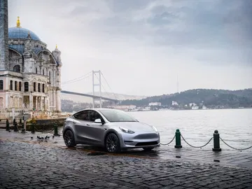 Tesla Model Y 2024 apreciado en su elegante perfil lateral con un paisaje urbano de fondo
