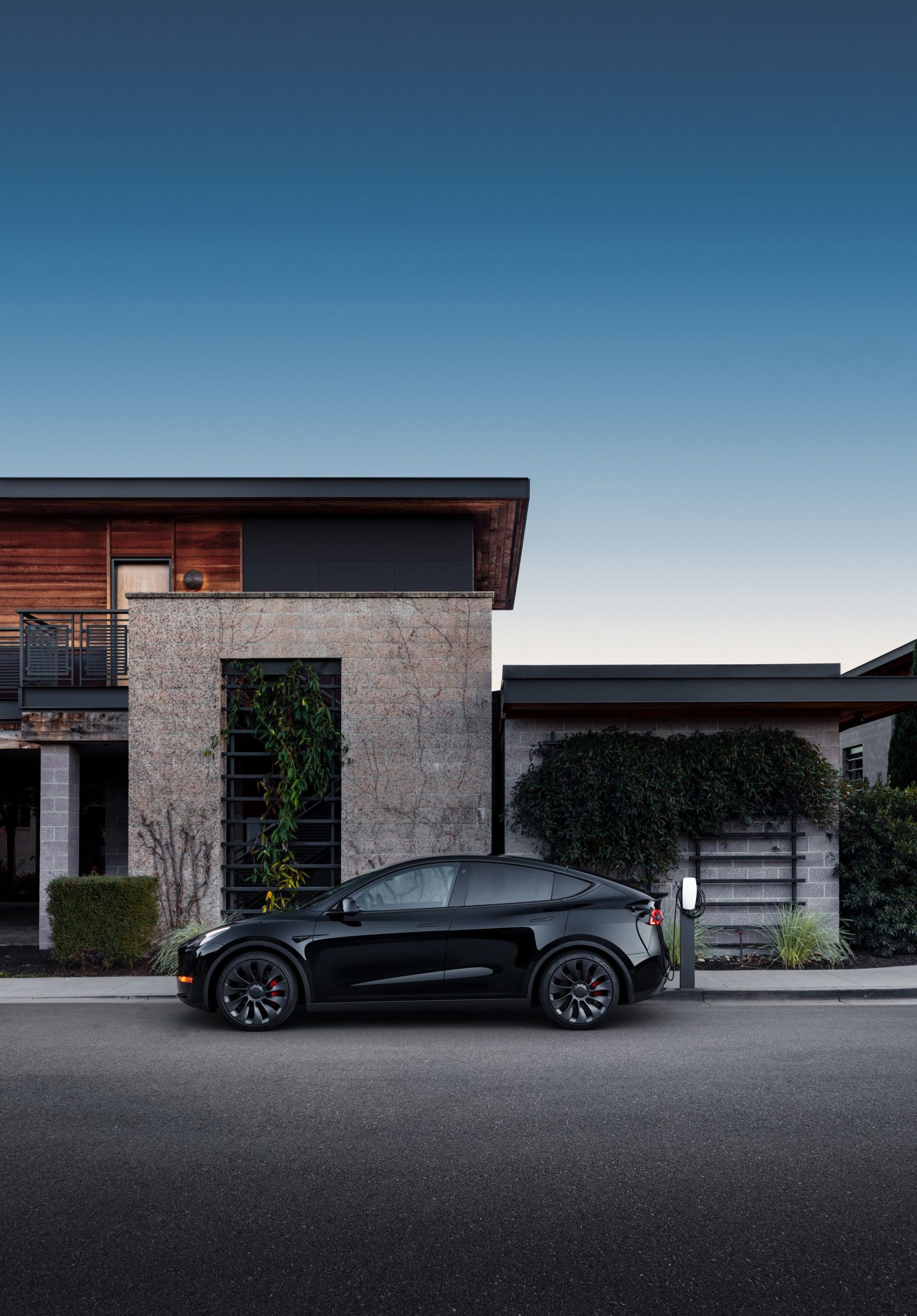 Vista lateral del Tesla Model Y 2024 estacionado frente a una residencia moderna