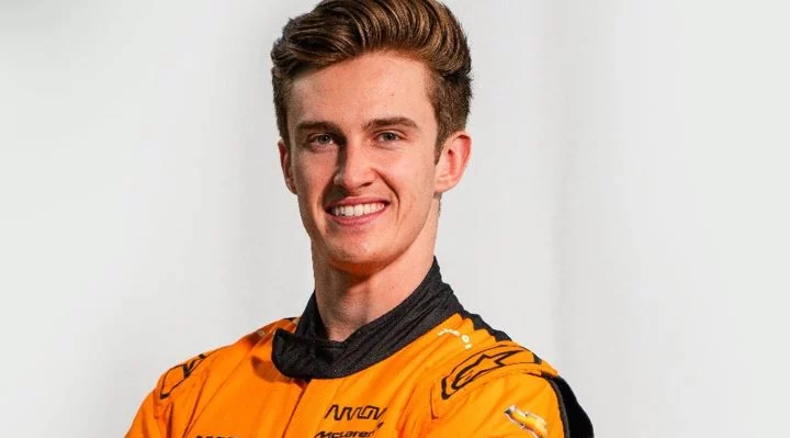 Piloto de Indycar con mono de competición McLaren, sonriente, enfoque de busto.
