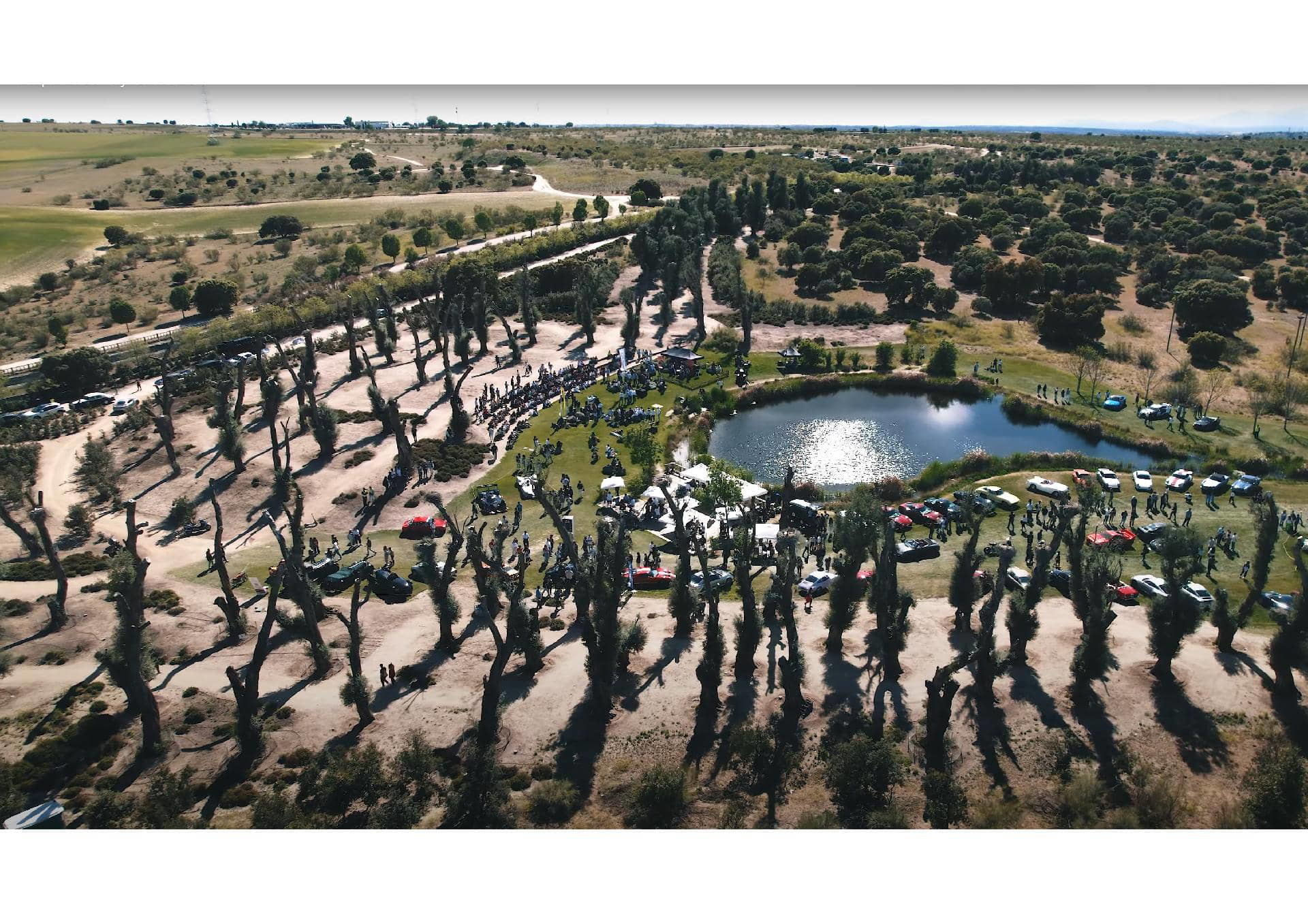 Vista aérea de una concentración de vehículos junto a un lago, ambiente perfecto para los entusiastas del motor.