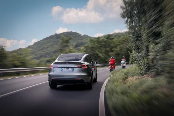 Vista dinámica del Tesla Model Y rodando en carretera, destacando su diseño trasero y lateral.