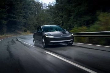 Vista dinámica de un Tesla Model 3 circulando por carretera húmeda.