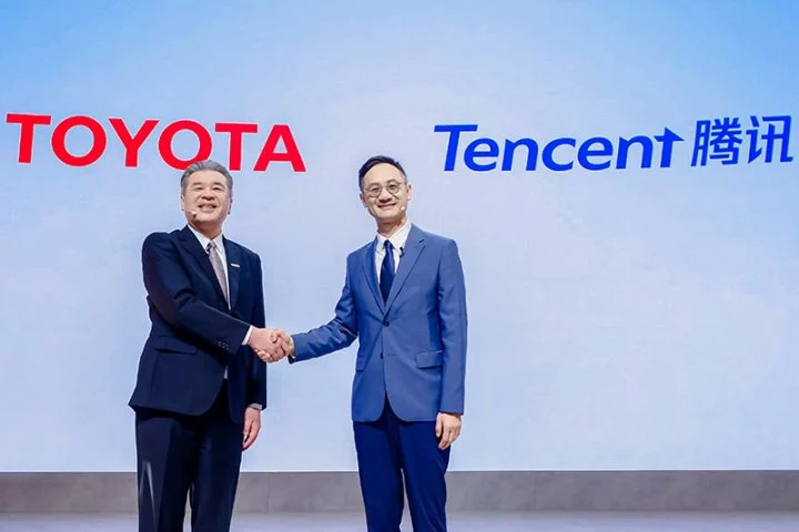 Dos ejecutivos estrechando manos frente a logos de Toyota y Tencent, simbolizando una alianza estratégica.