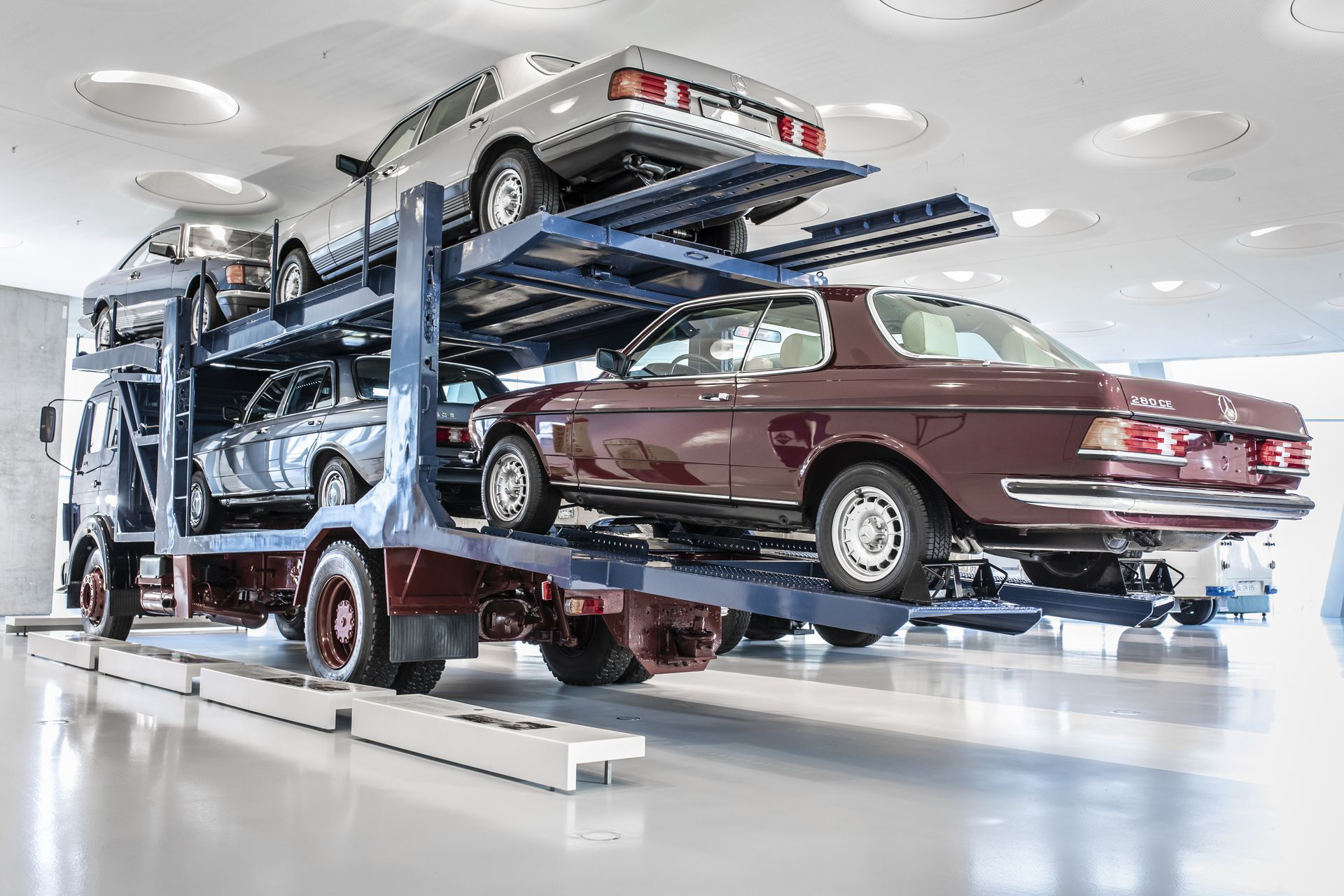 Vista lateral de un portacoches Mercedes 1624 cargado con vehículos clásicos.