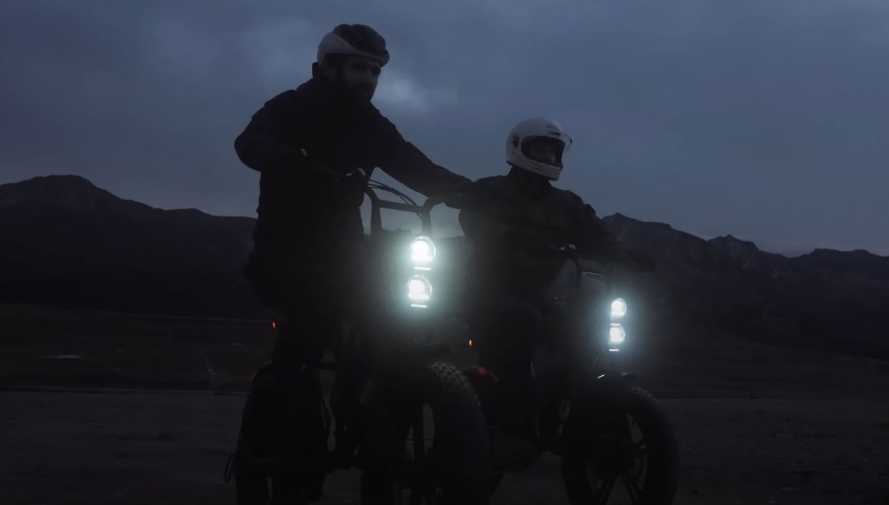 Dos e-bikes estilo scrambler destacando su iluminación delantera.