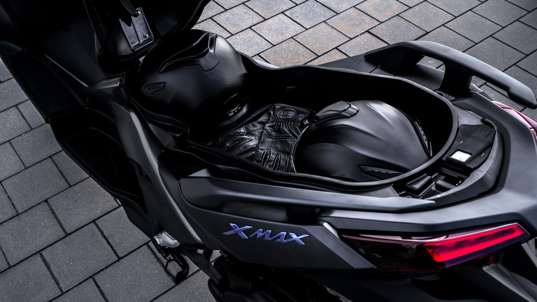 Vista trasera-lateral Yamaha X-Max 125cc que muestra su diseño aerodinámico y acabados premium. Vista trasera-lateral Yamaha X-Max 125cc que muestra su diseño aerodinámico y acabados premium.
