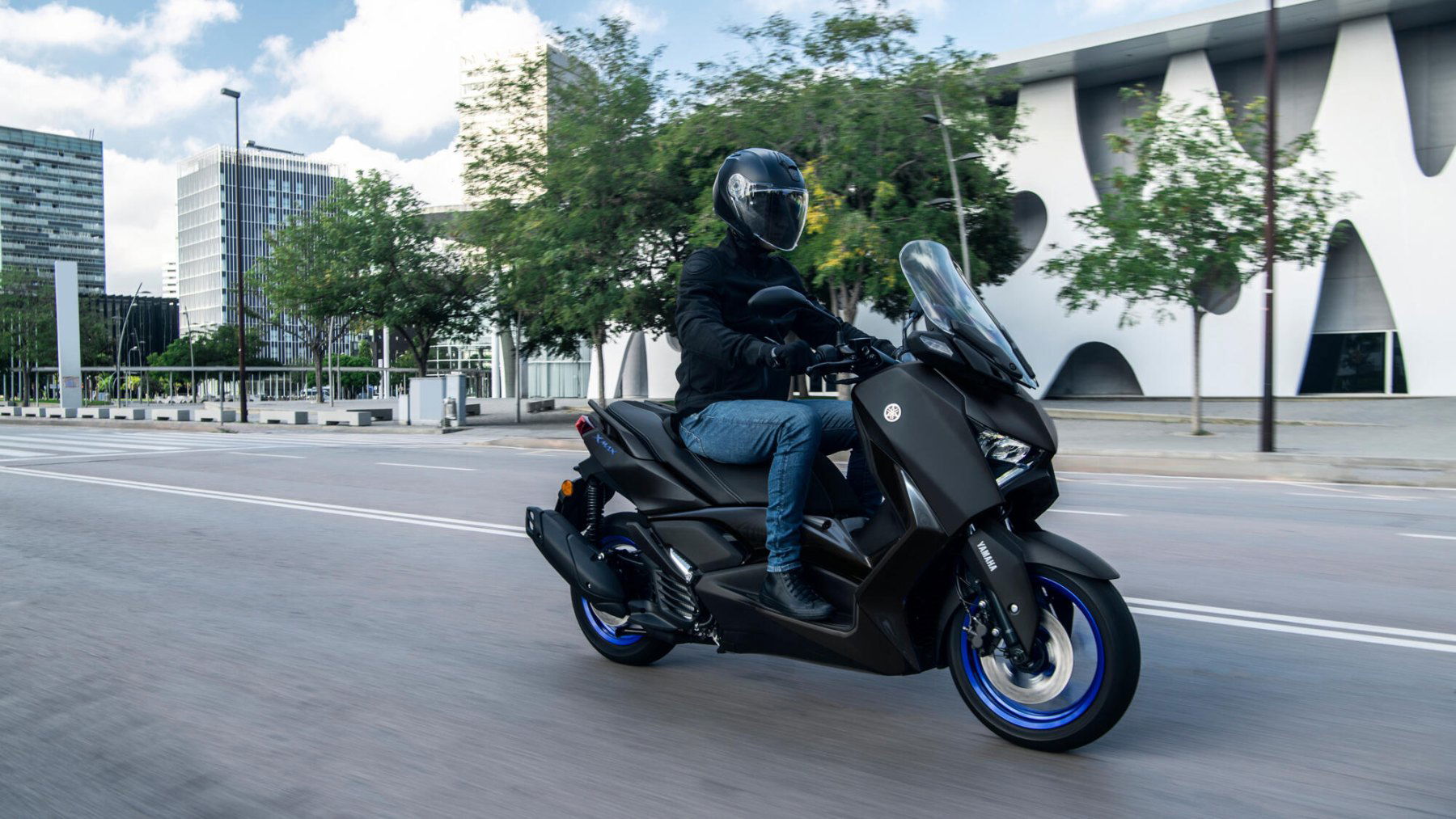 Vista lateral del Yamaha X-Max 125cc en movimiento por la ciudad. Vista lateral del Yamaha X-Max 125cc en movimiento por la ciudad.