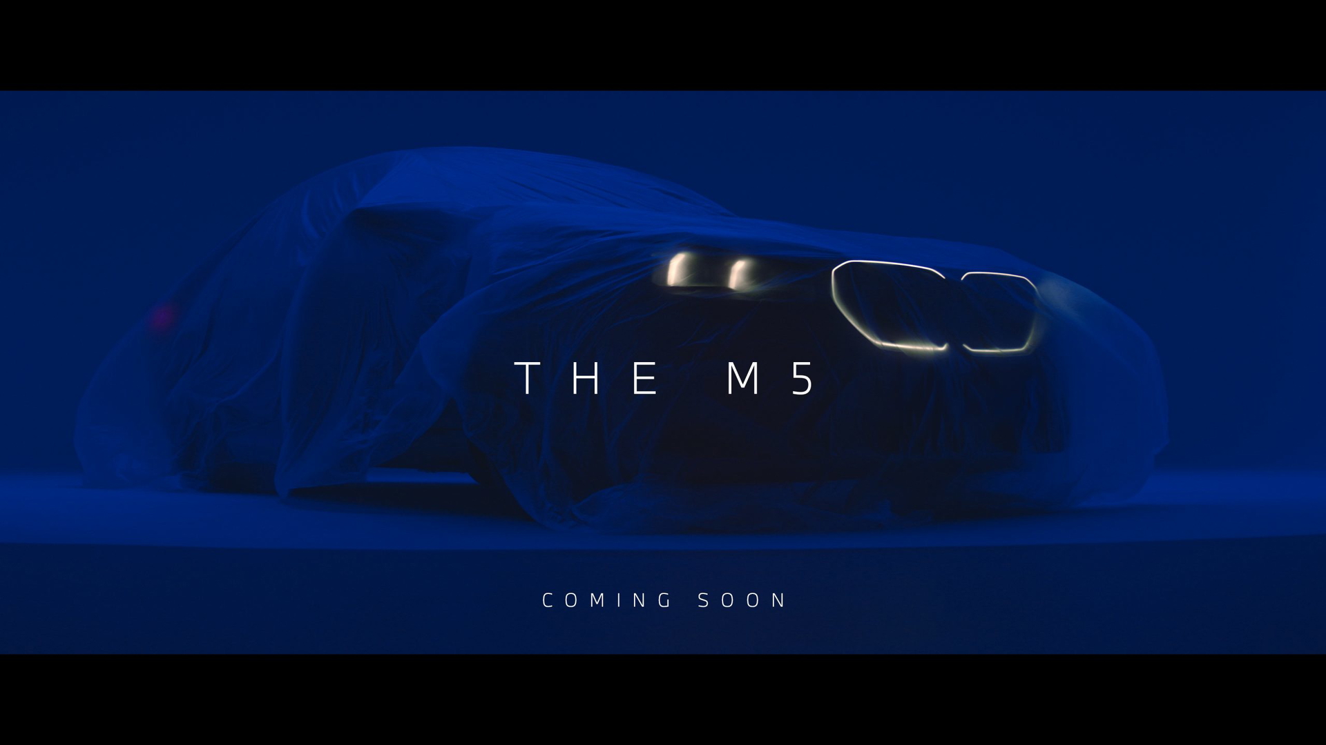 Vista anticipada de la delantera del nuevo BMW M5 bajo manto, prometiendo gran potencia.
