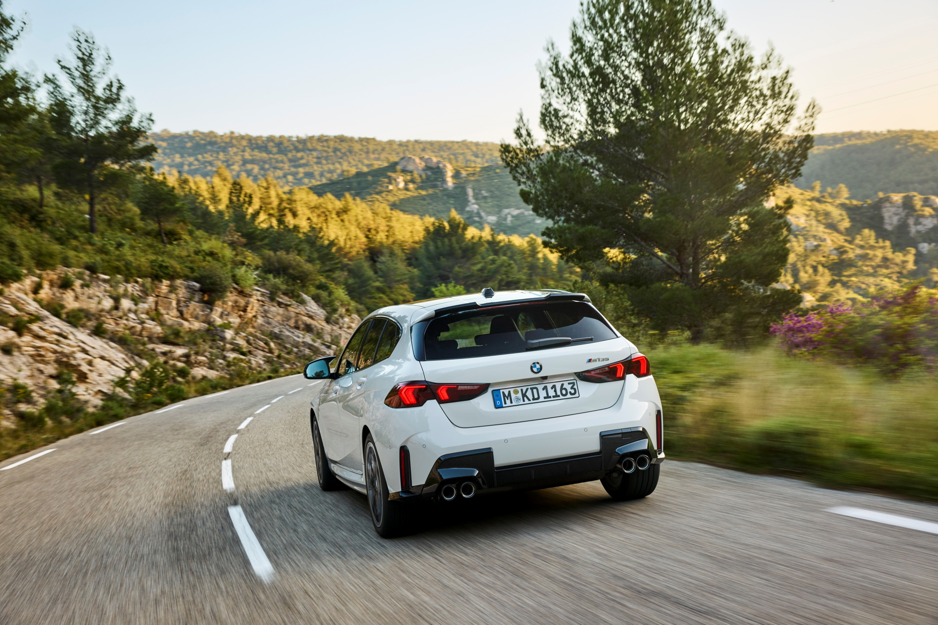 Vista trasera del nuevo BMW M135 en movimiento, mostrando su diseño deportivo y dinámico.