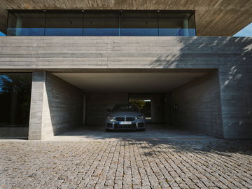 La trasera y el lateral de un BMW M2 se destacan bajo una moderna estructura de concreto.