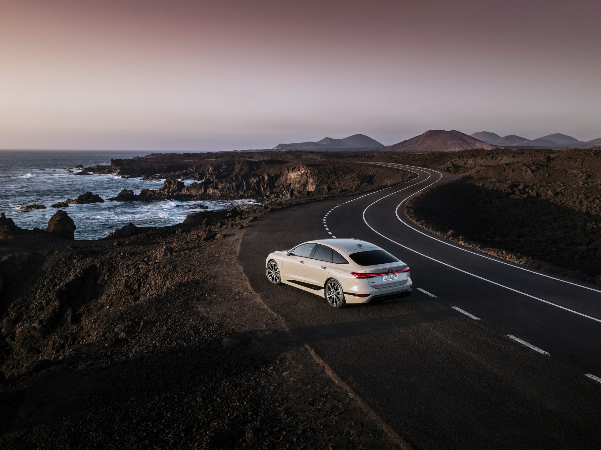 Audi A6 e-tron 2024 navegando por la carretera costera al atardecer.
