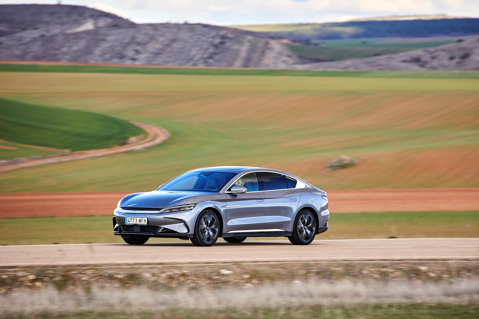 Perfil de coche eléctrico en carretera con paisaje campestre
