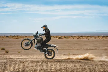Motorista realizando una maniobra de salto con una trail potente en terreno arenoso.
