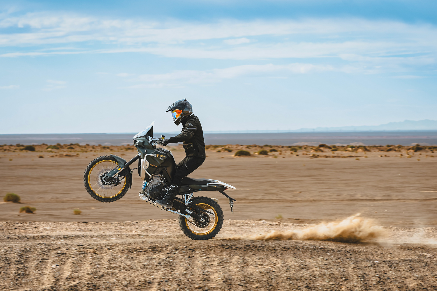 Motorista realizando una maniobra de salto con una trail potente en terreno arenoso.