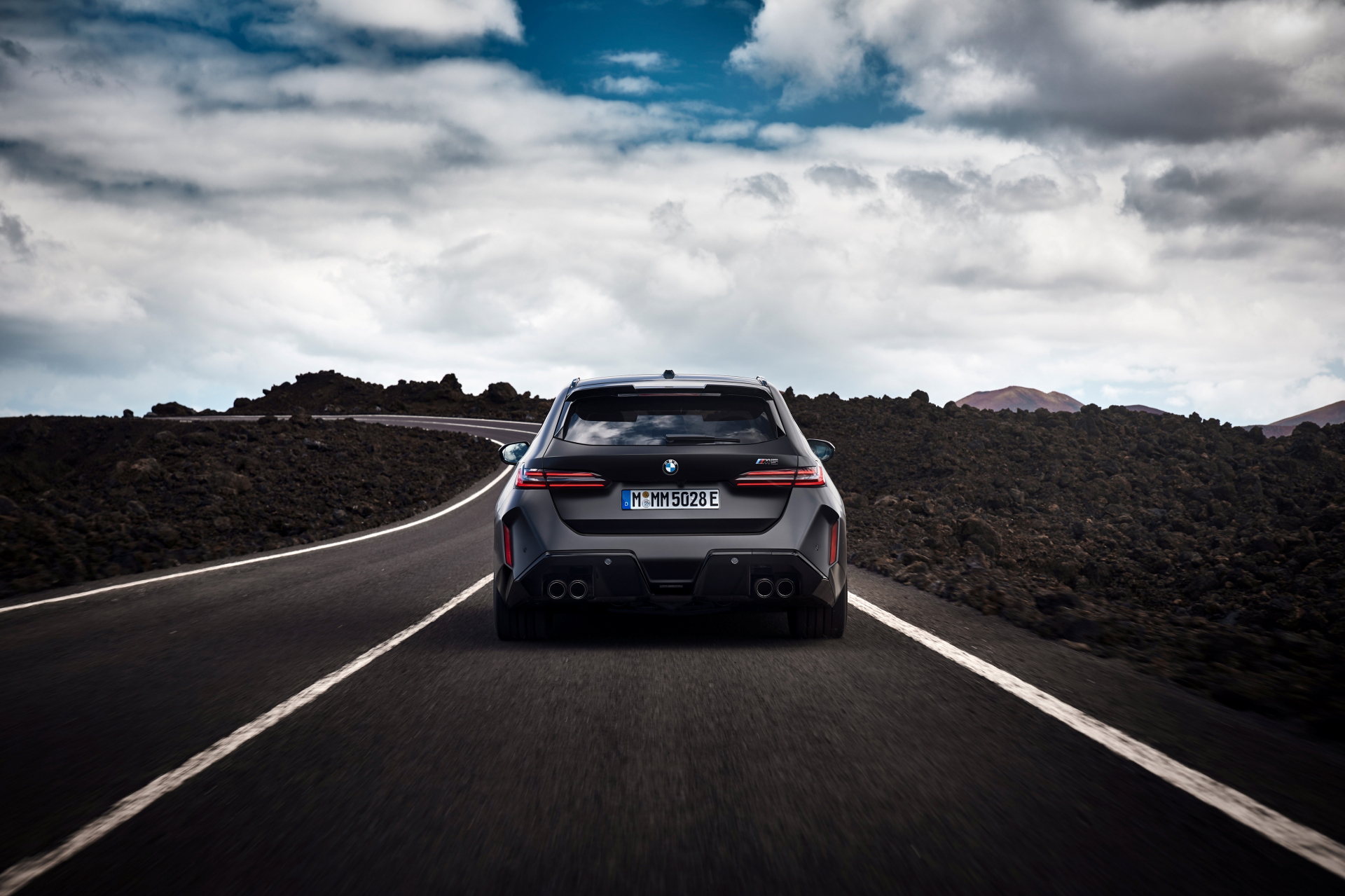 Vista trasera del BMW M5 Touring 2025 en carretera, mostrando su diseño y deportividad.