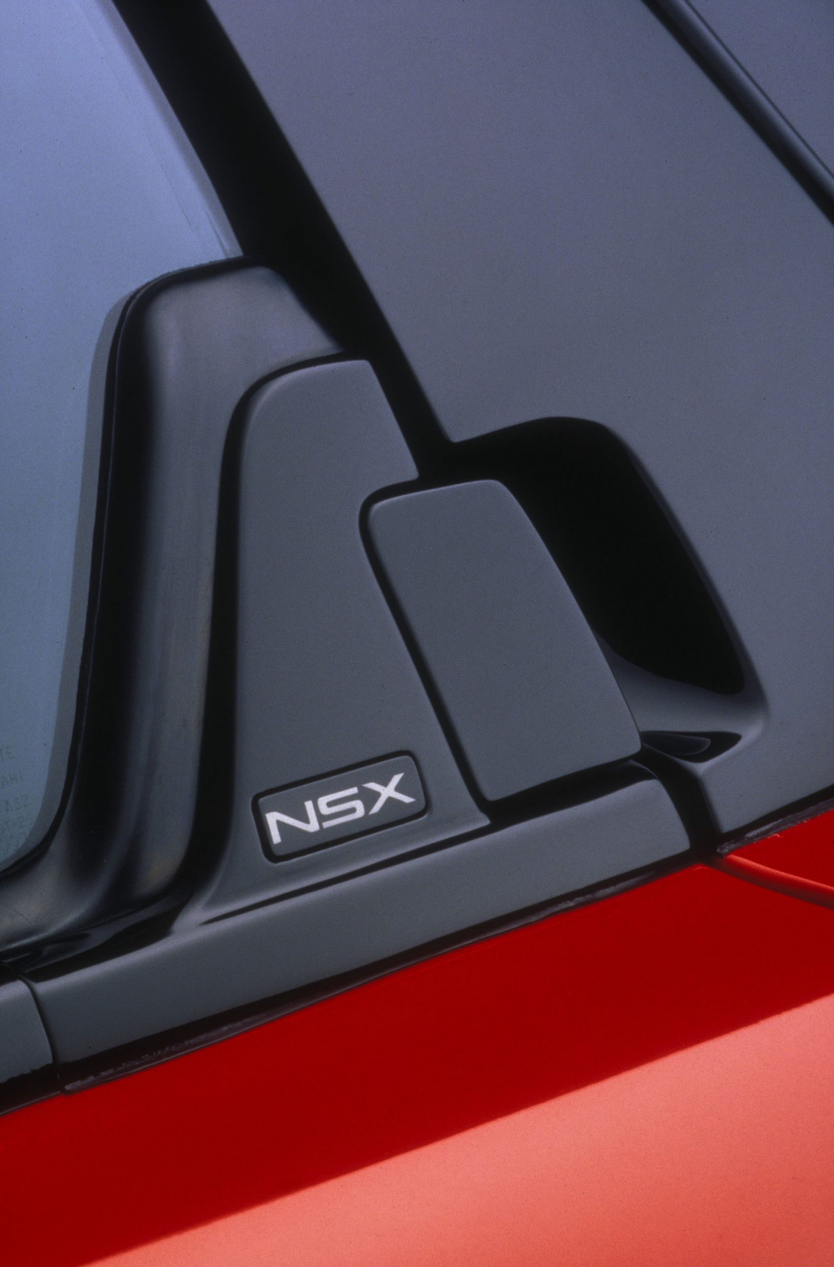Vista parcial de la insignia NSX sobre carrocería roja y negra, icónica del deportivo.