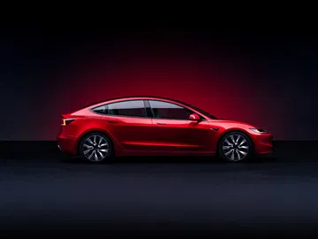 Perfil lateral de Tesla Model 3 en rojo bajo iluminación tenue.