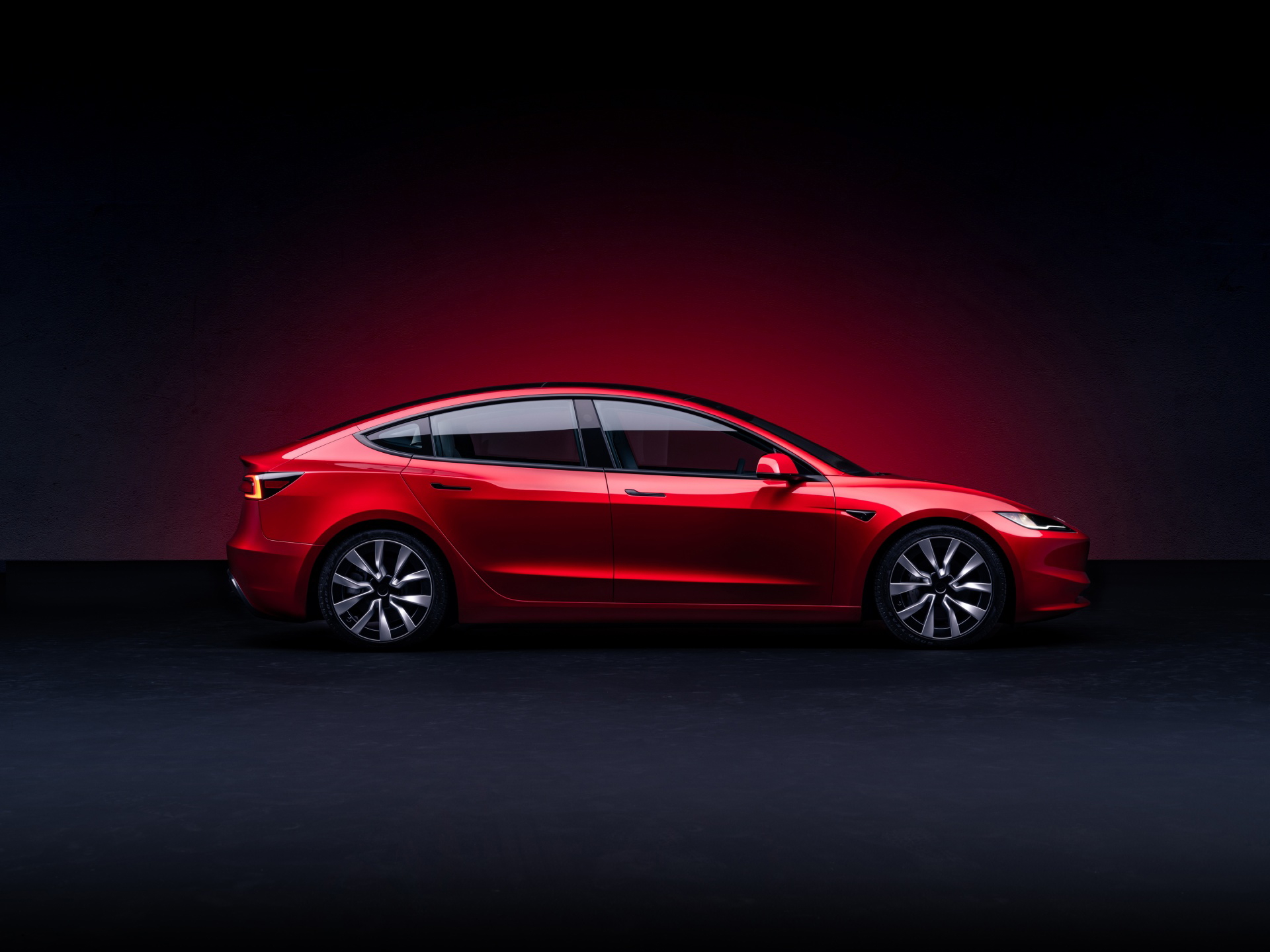 Perfil lateral de Tesla Model 3 en rojo bajo iluminación tenue.