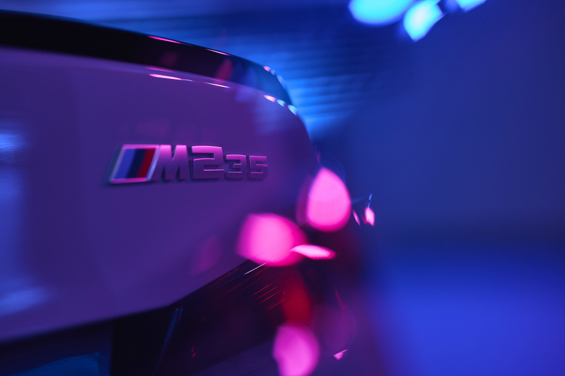 Vista trasera enfocando el emblema M235i de BMW en ambiente iluminado.