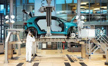 Empleados trabajando en Volkswagen, con carrocería de coche en ensamblaje.