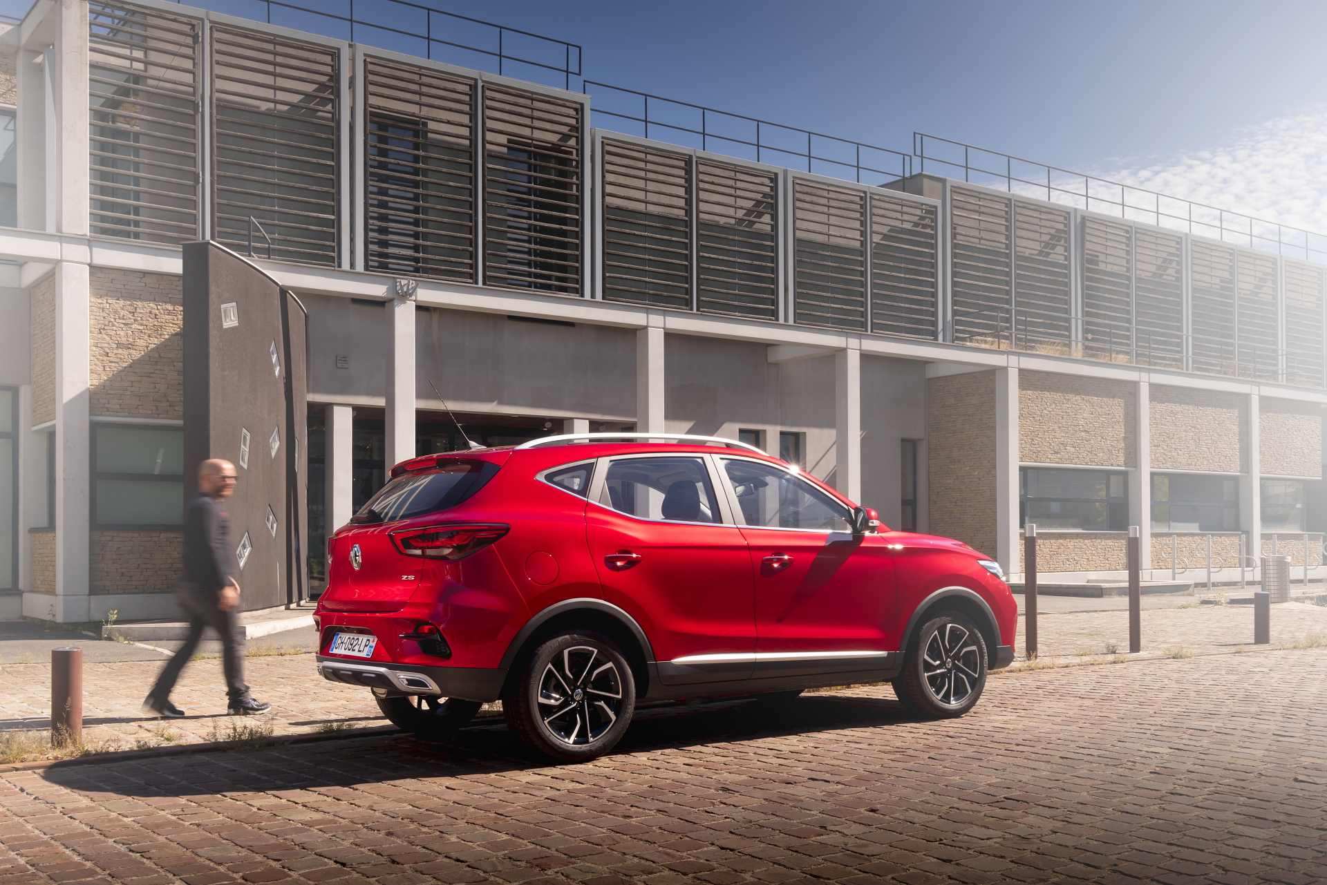 El MG ZS rojo muestra su diseño lateral cerca de un edificio moderno.