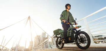 Vista lateral de la e-bike UBCO 2x2 con piloto a bordo en entorno urbano