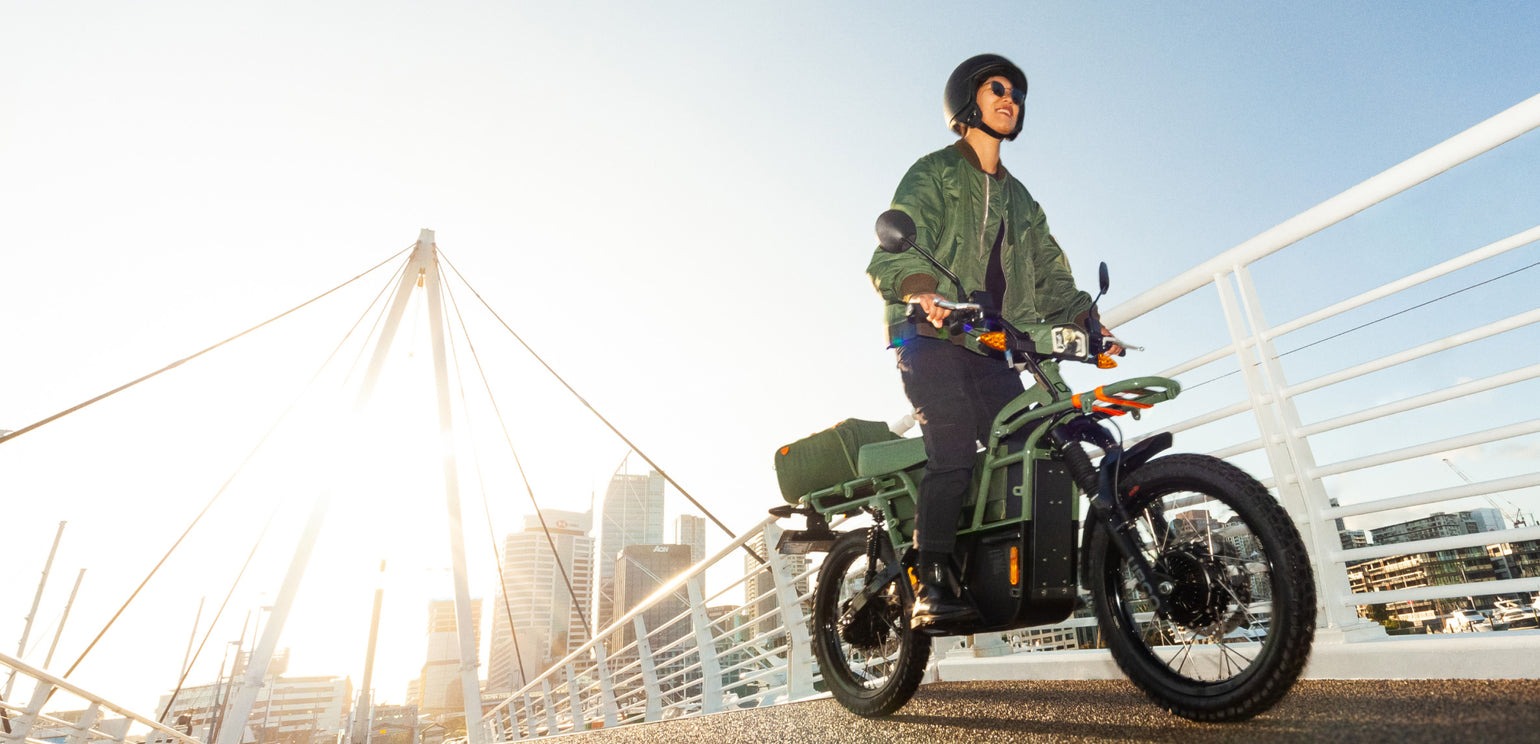 Vista lateral de la e-bike UBCO 2x2 con piloto a bordo en entorno urbano