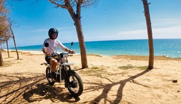 Vista lateral de la UBCO 2X2 eBike en un entorno playero con conductor.