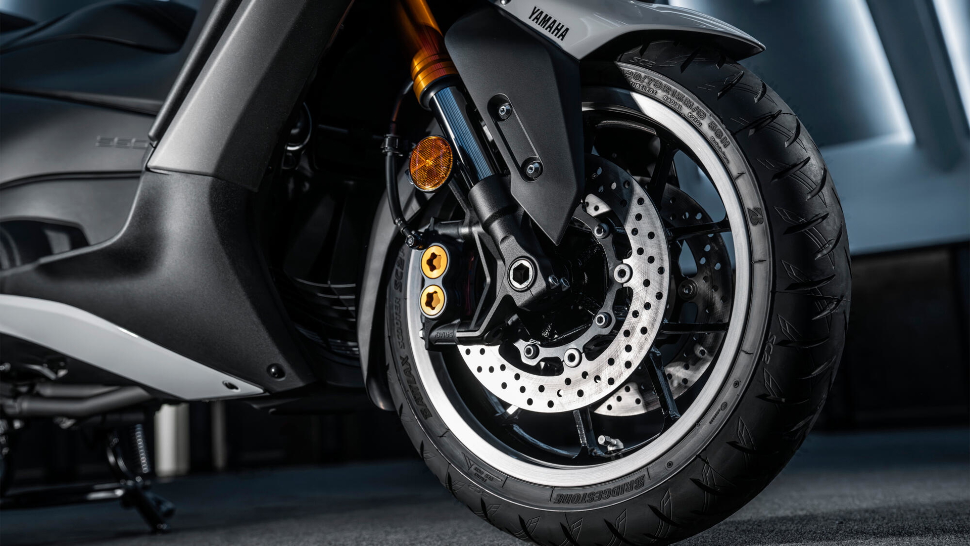 Vista lateral de la Yamaha TMAX 2025, enfocando el detalle de las llantas y frenos.