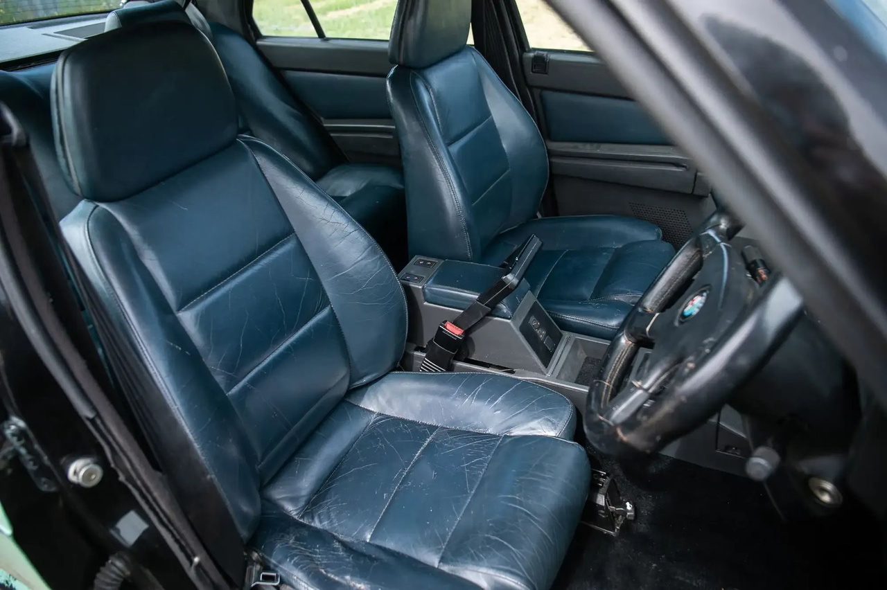 Interior del Alfa Romeo 75, mostrando unos asientos de cuero azul con signos de desgaste.