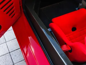 Vista detallada del interior del Ferrari F40 LM, resaltando su asiento deportivo rojo y elementos de carbono.